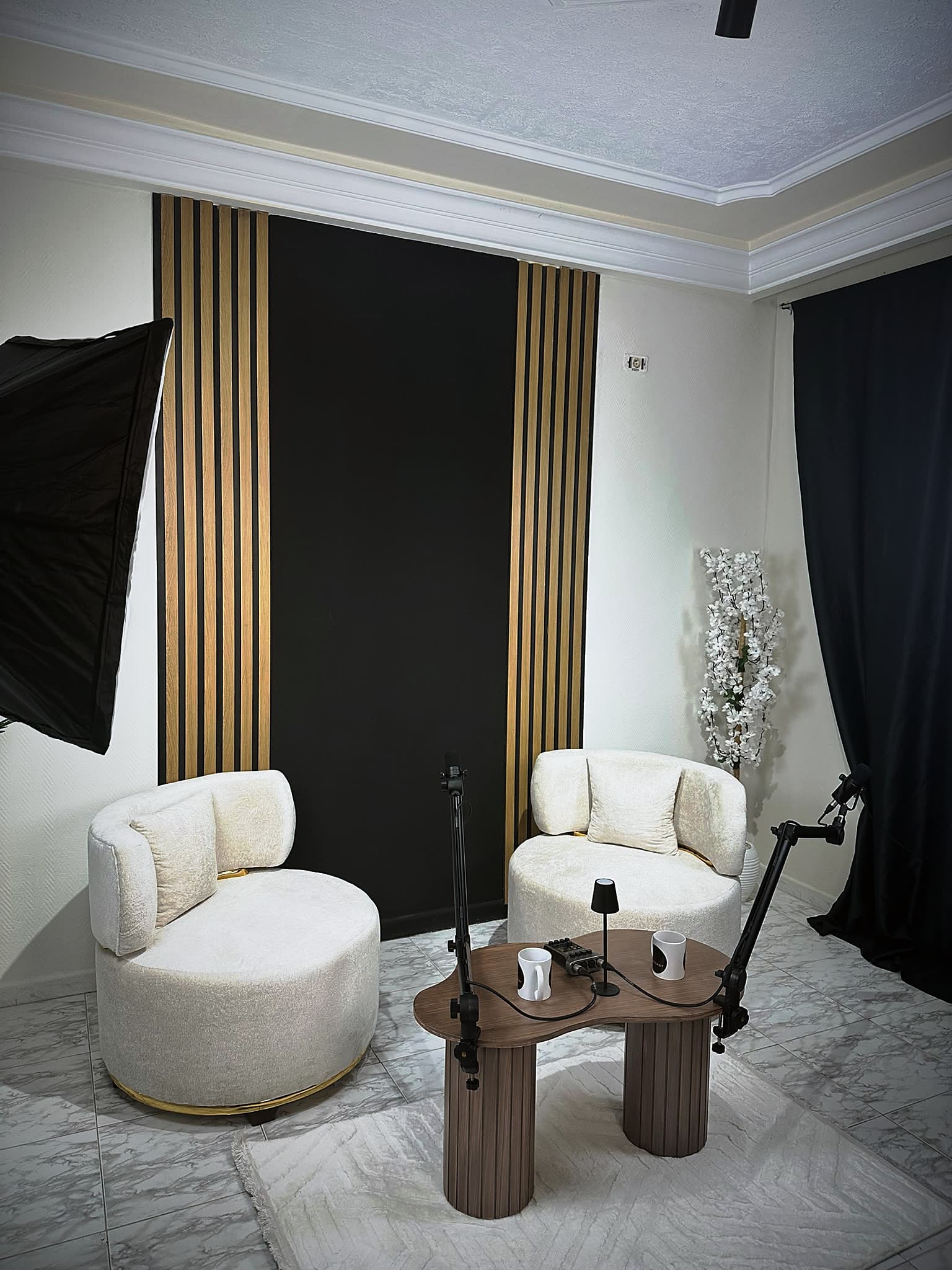 White lounge chairs and a wooden table with microphones in front of a slatted wall