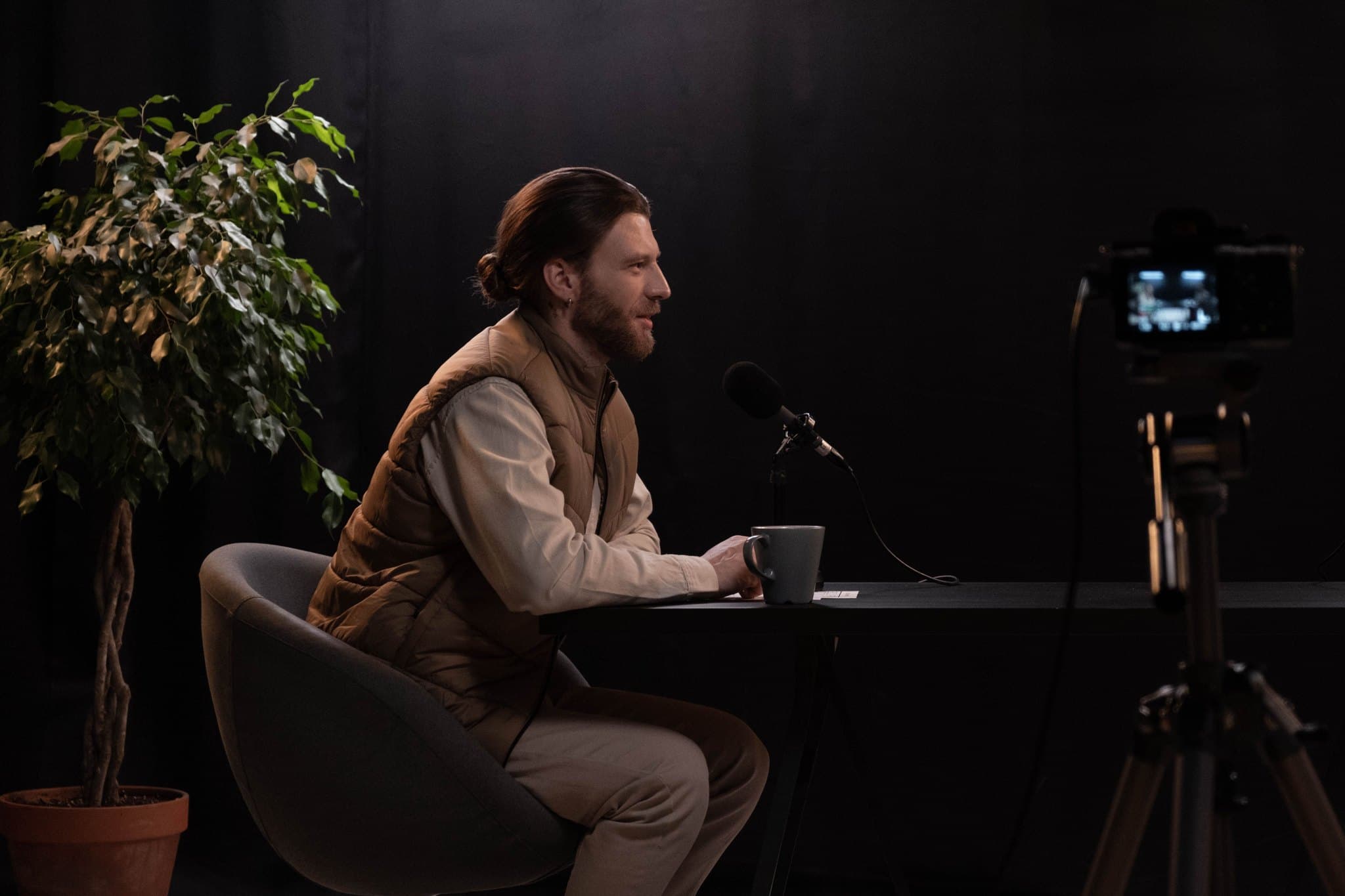 Creator recording a podcast at a desk mic, with a camera filming him in the studio